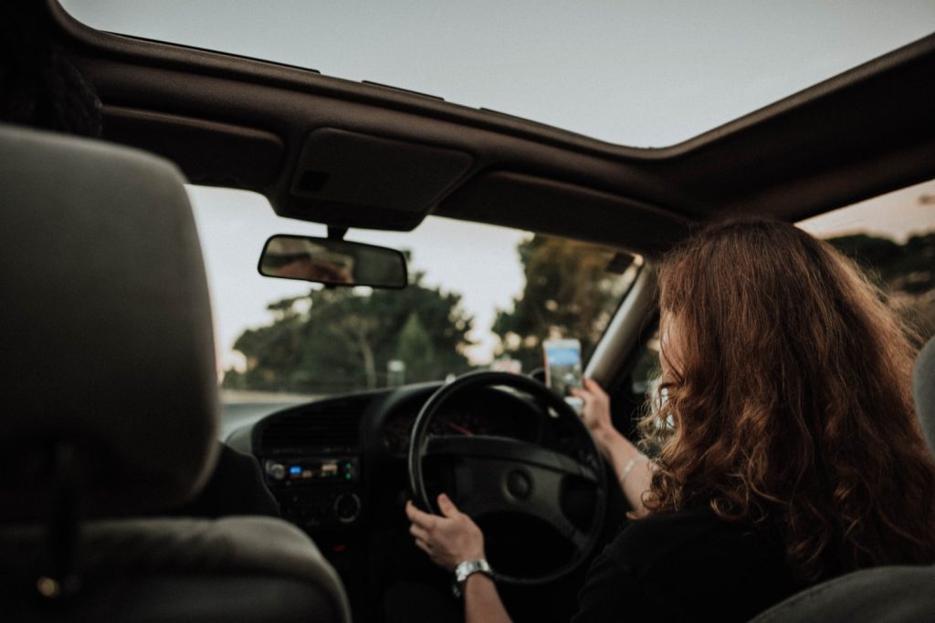 woman driving while taking a picture with her smart phone