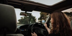 woman driving while taking a picture with her smart phone